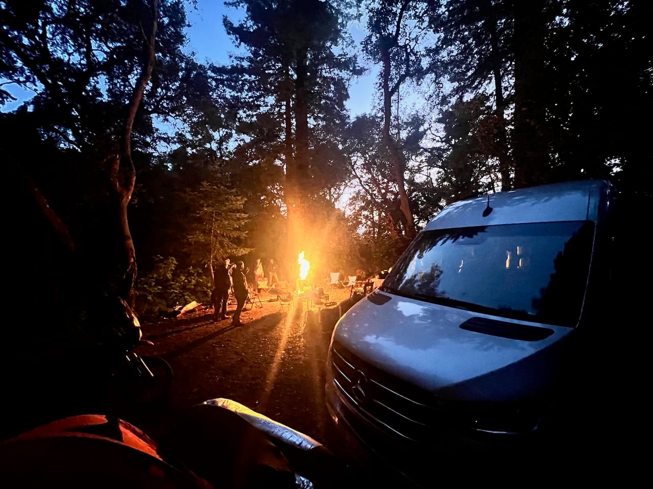 The van at a forest campsite with the sun setting through the trees